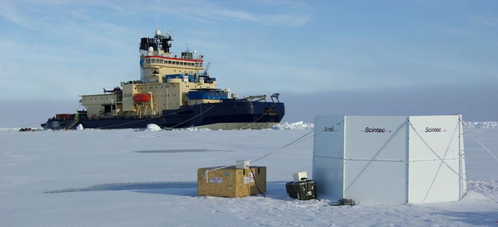 Large blue and white ship rests in a large ice platform behind boxes of scientific equipment