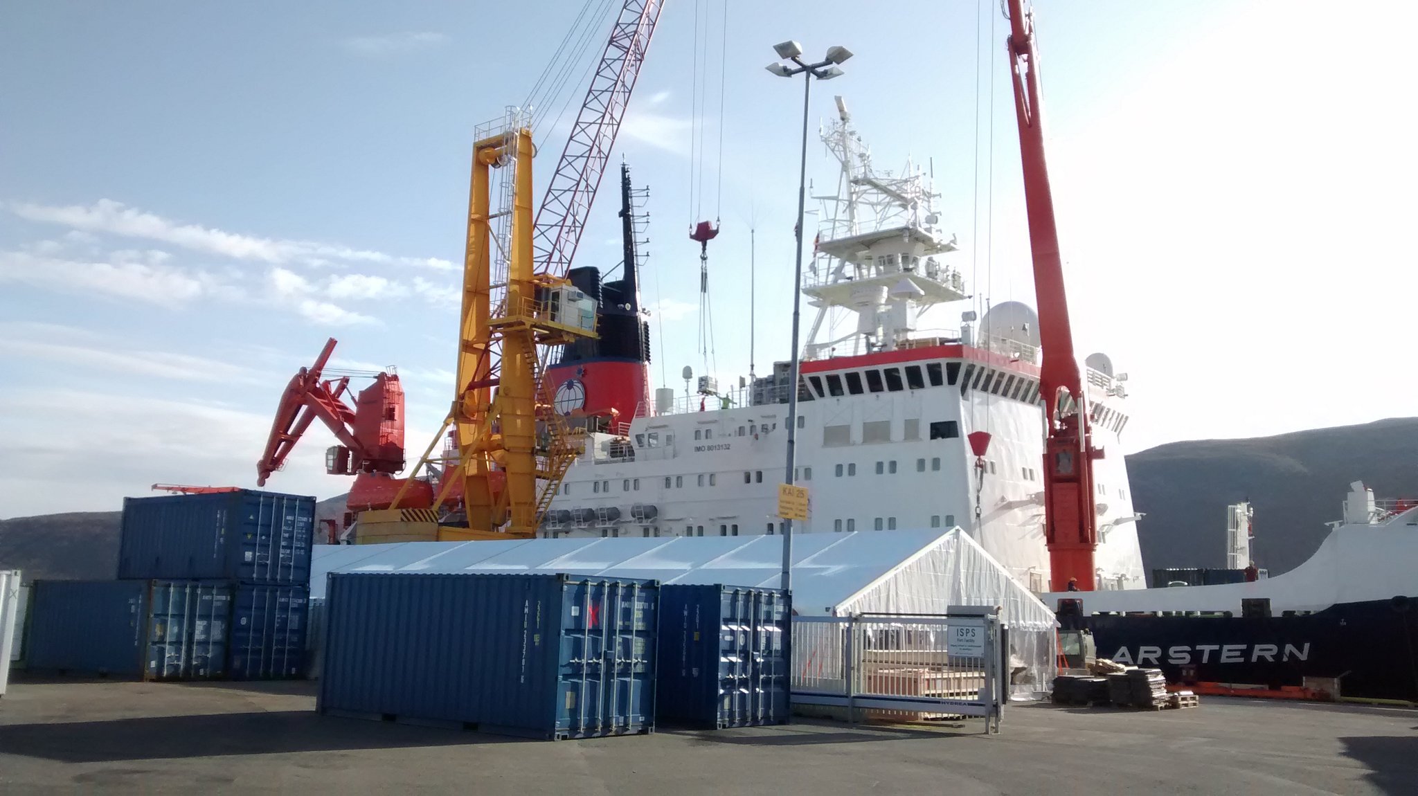 Orange crane moves blue shipping container onto a large white icebreaker ship